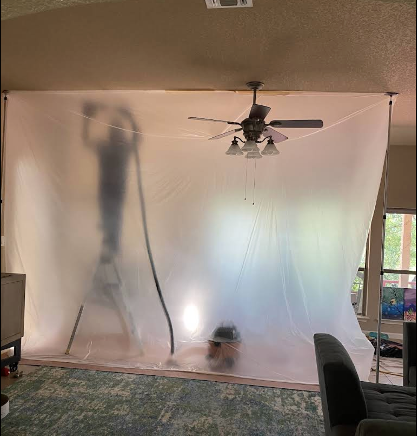 Roland applying drywall texture behind a protective plastic barrier during a popcorn ceiling removal job